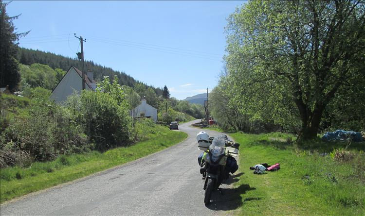 The bikes near the white scottish houses surrounded by steep tree covered hills and blue sky