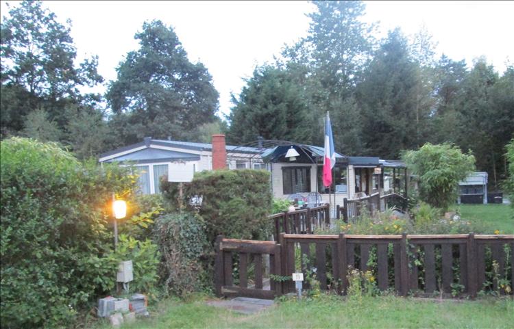 A static caravan on a plot with extensions and fences and flags and a chiminea