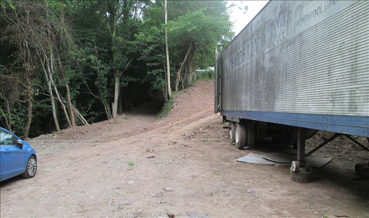 a broad dirt track leads up behind an abandoned lorry trailer at the working farm