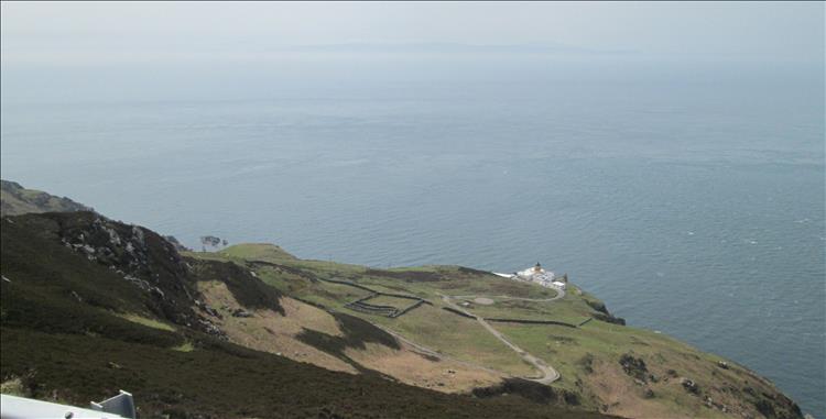 The lighthouse at the bottom of the steep hill, misty sea waters and maybe we can see ireland in the distance