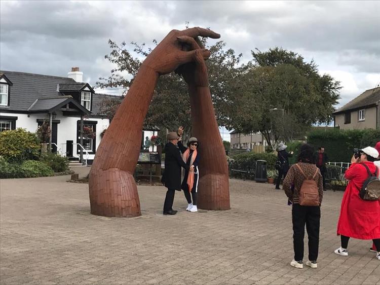 2 giant forarms with hands tower over a Japanese couple at gretna