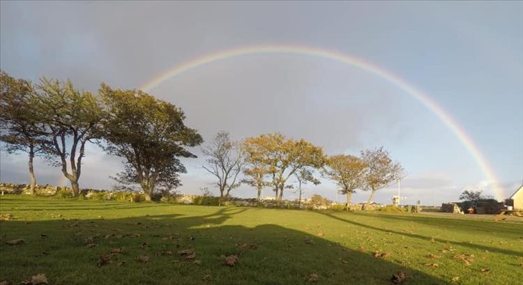A vivid narrow rainbow over the green grass at the campsite