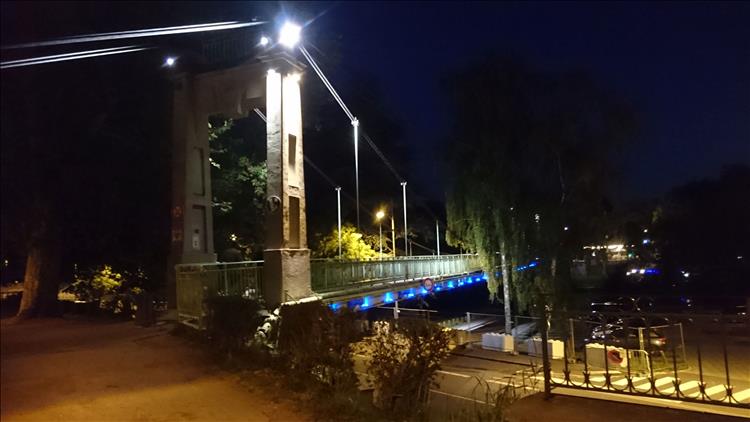 The iron and stone suspension bridge, illuminated in the dark evening
