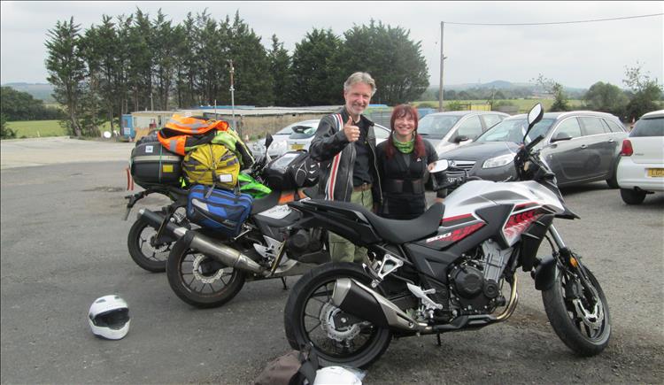 Ross and Sharon stand behind Ross's shiny CB500X motorcycle giving us the thumbs up