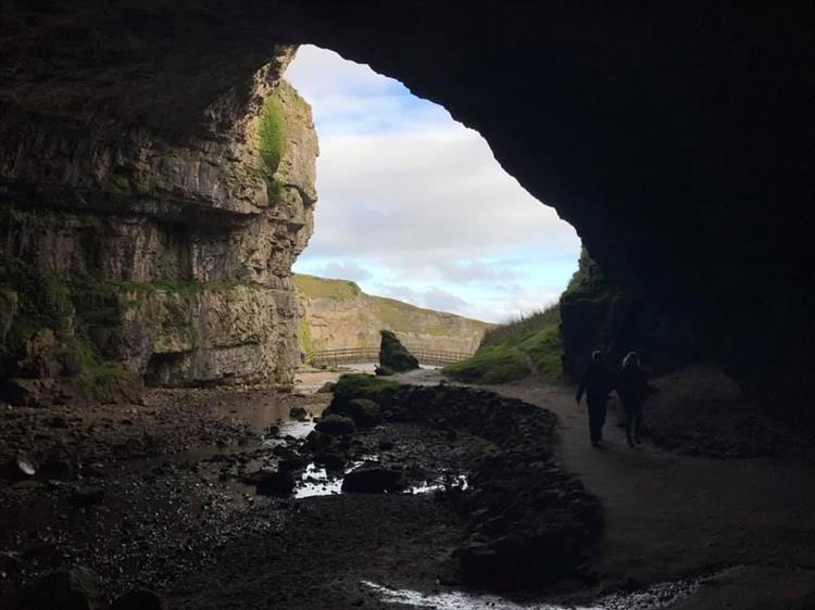 Looking out from the dark cave to a steep and rocky cove at smoo cave