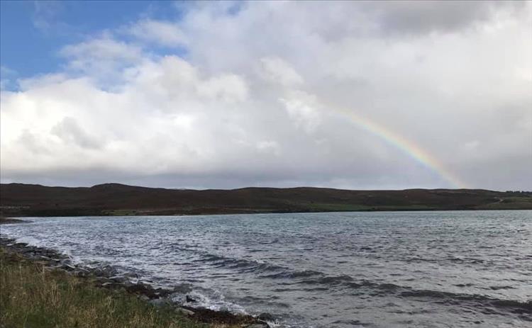 A rainbow carves across the sky ending in a hill by the shores of a loch in Tongue, Scotland