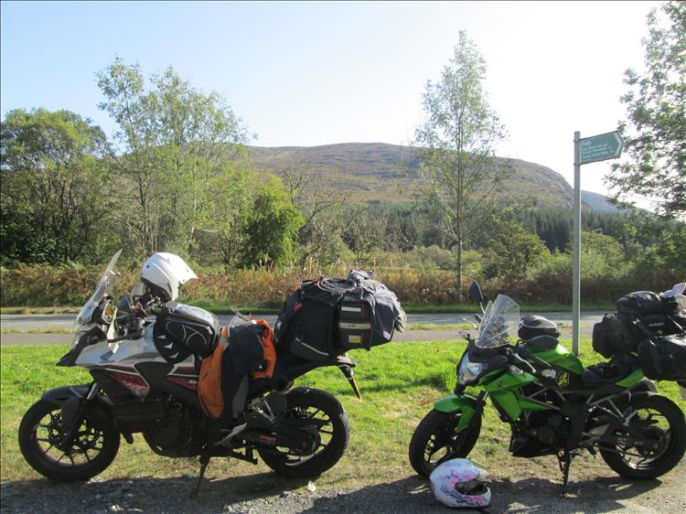 The motorcycles with luggage by the roadside with hills and trees in the background