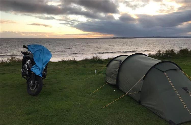 The BMW motorcycle and tent by the shore under mixed skies in the early morning