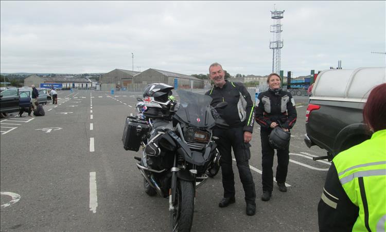 A couple dressed in black cordura bike gear smile stood by their BMW Adventure bikes