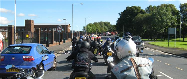 A large group of riders wait on the road during an organised event