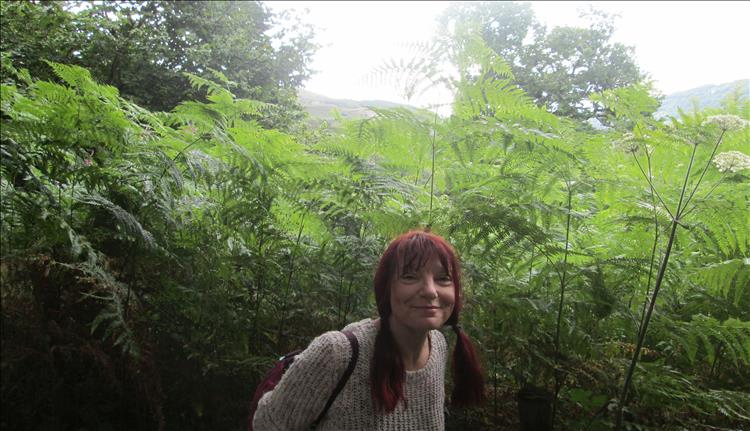 Sharon smiles, behind her are tall almost prehistoric ferns