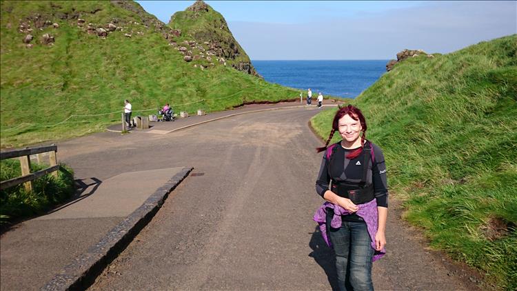 Sharon smiles with the sun in her eyes as the road leads down between grassy outcrops