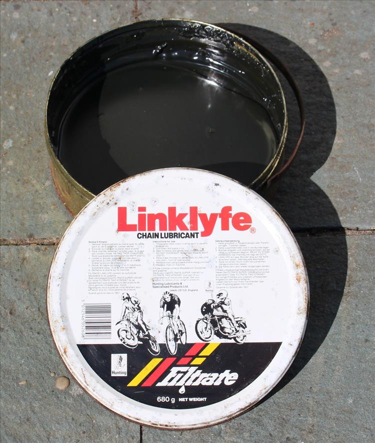 A round tin, about 6 inch diameter with a black tar like substance, with the LinkLyfe tin lid beside it