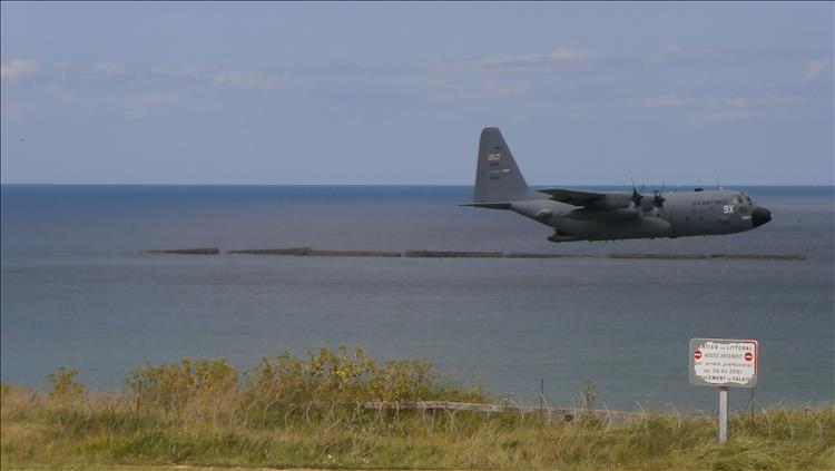 A large C130 4 prop transport plane flying very low just off shore at the Normandy Beaches