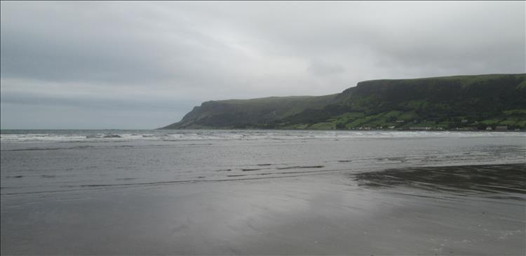 A broad, wide sandy beach with the hills jutting into the sea in the distance on a rather grey afternoon