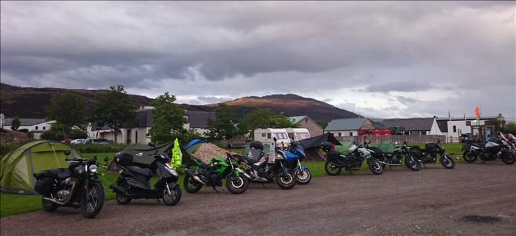 A line of motorcycles in front of various tents on the campsite in Ullapool