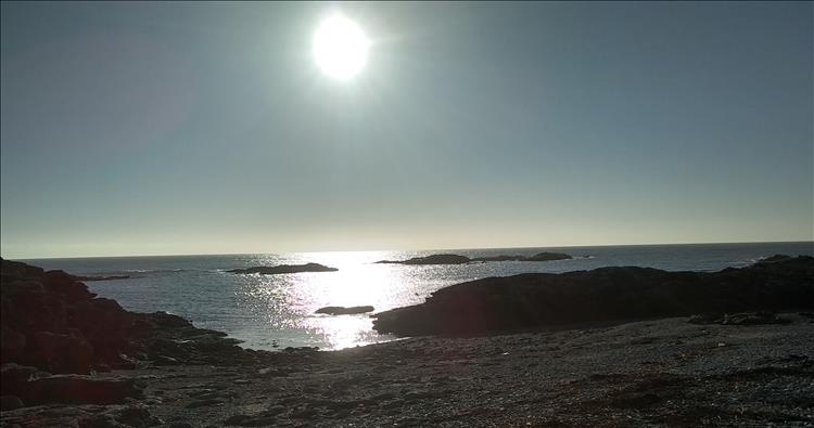 Bright sun and clear skies over rocky outcrops and stony beach at Trearddur Bay