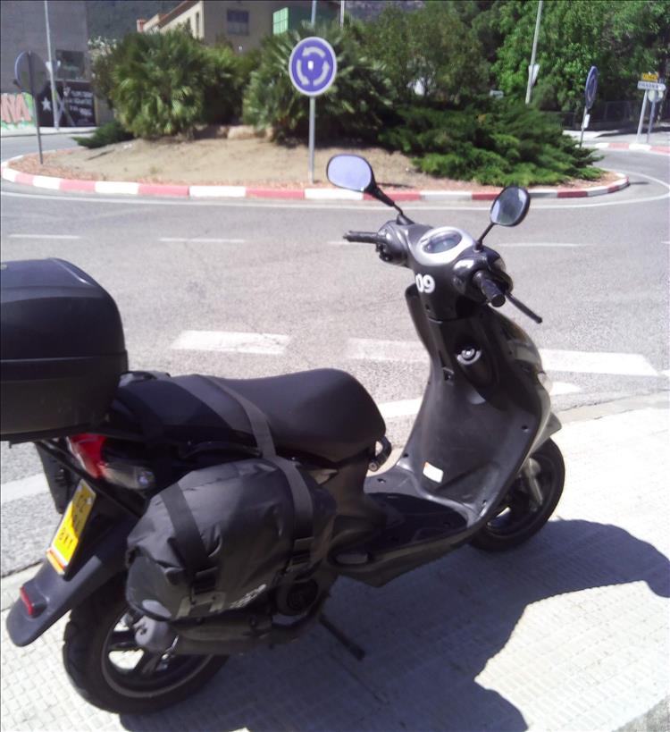 A black scooter with saddle bag by a roundabout in sunny spain