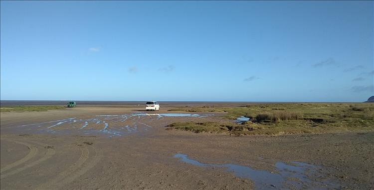 A broad sandy parking area and clear blue skies at Lon-Y-Traeth