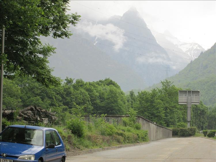 A misty massive mountain, a road and a car in the French Alps