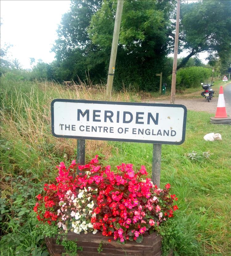 The sign for Meriden, above a vivi red flower bed and among grasses and trees