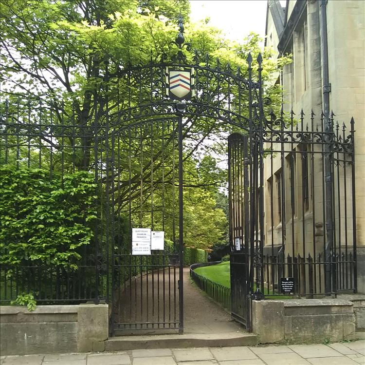 Metal railings and gate then a footpath and grass down the side of a stone building