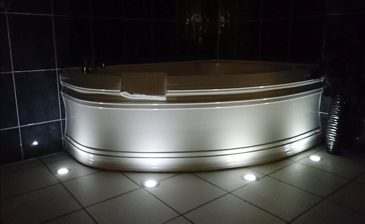 The oval bath is subtly lit from the floor with dark tiles and excellent finish