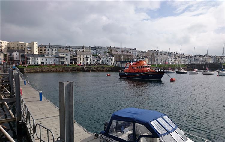 A large bright orange lifeboat is safely moored in the calm waters at Portrush Harbour