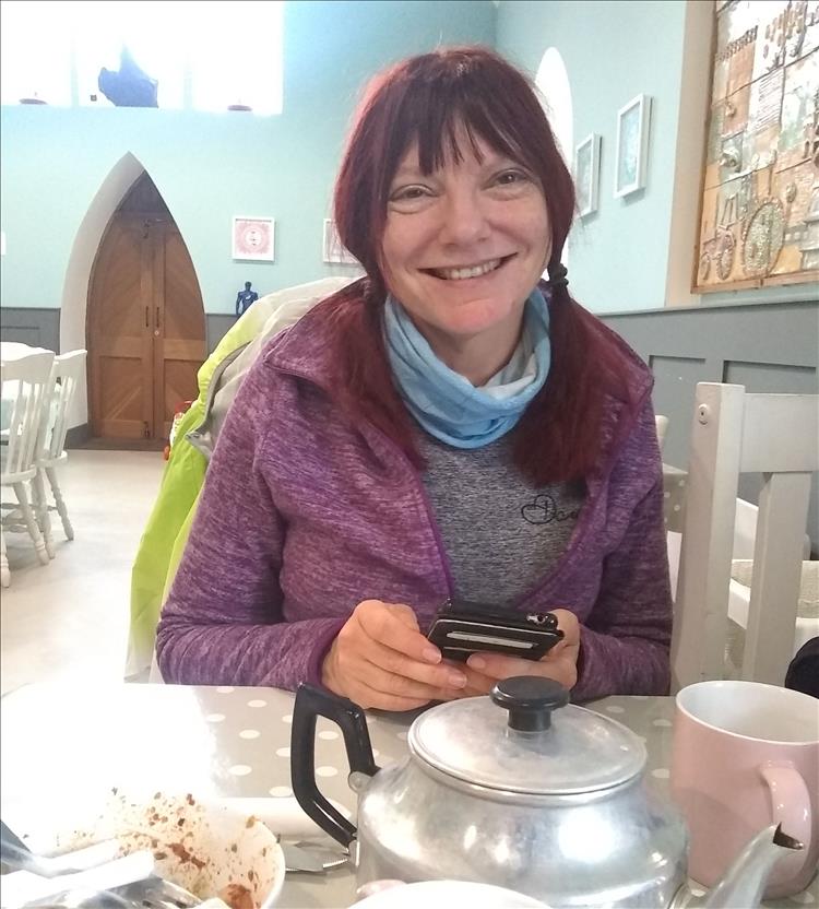 Sharon smiles and in front of her we see a teapot and the empty bowl of chilli chips