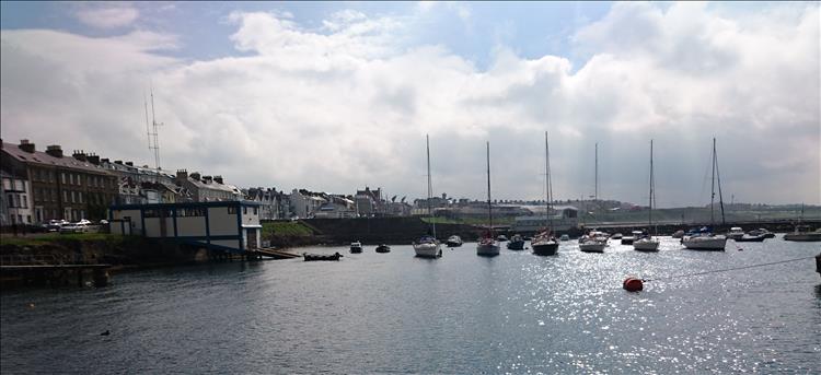 In a gap in the clouds the sun shines down on the waters, boats walls and surrounding houses at Portrush harbour