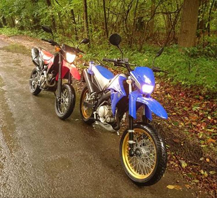 2 supermotard style motorcycles park by the road on a wet day