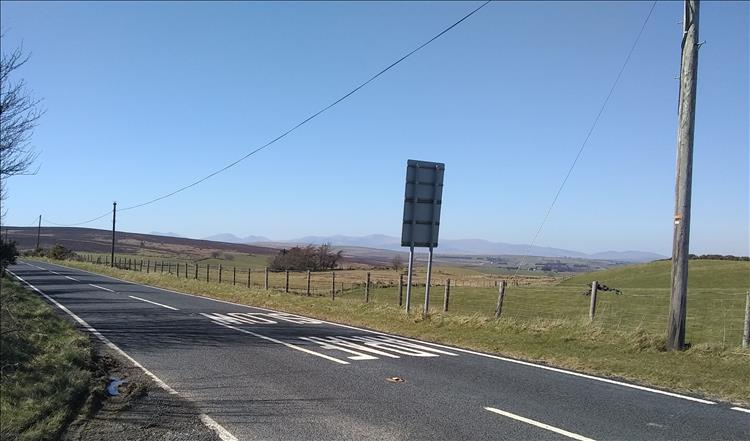 Clear blue skies, the road and in the far distance the jagged tips of the Snowdonian mountains