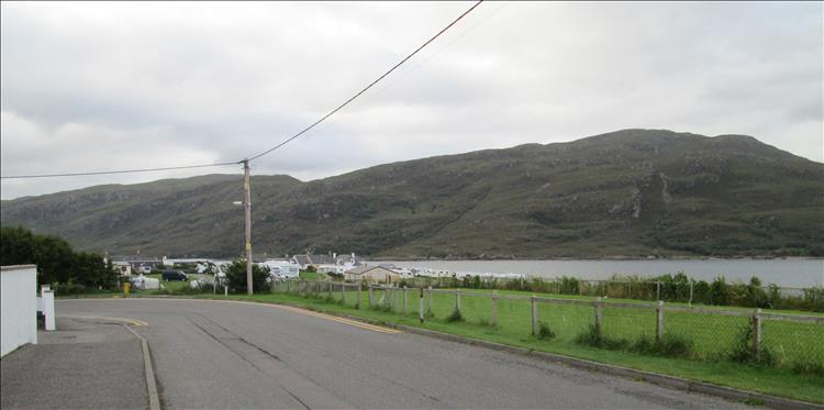 Ullapool we see a road, some houses and grassy areas and the mountains a loch behind