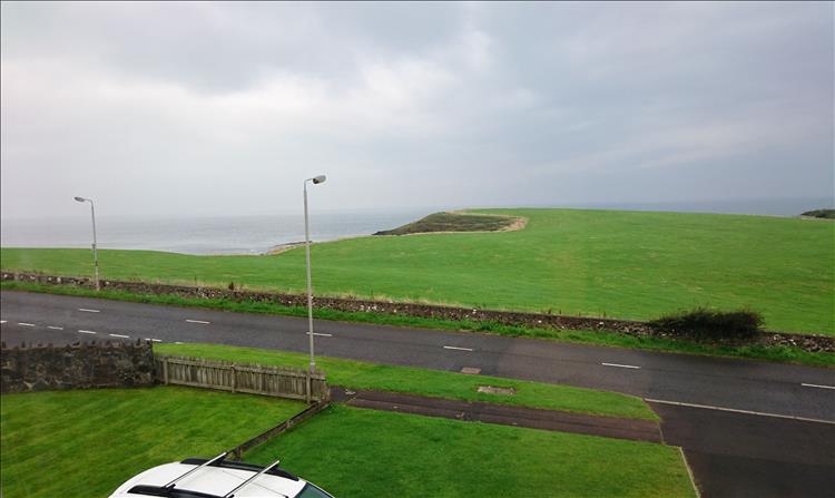 Looking from the upper floor of the house we see green grass leading to bluffs and the sea with grey skies