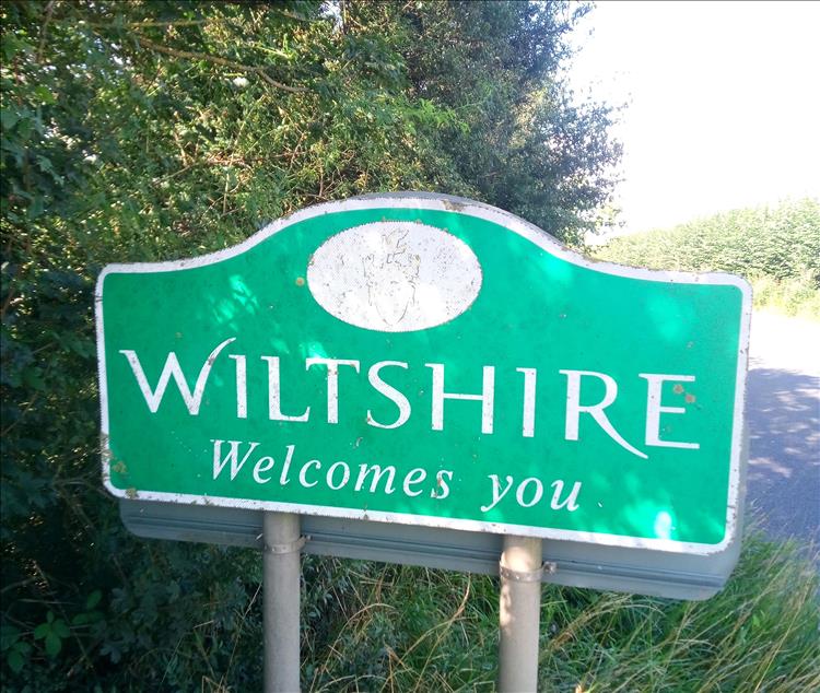A welcome to Wiltshire sign beside the road in the trees