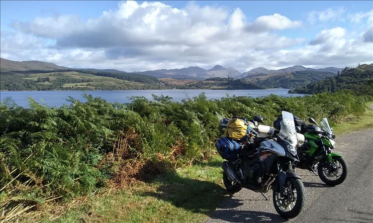 The bikes are close to the camera, behind we see the loch and many mountains in the distance