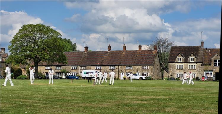 Cricket on the village green, trees and old stone houses in a perfick scene