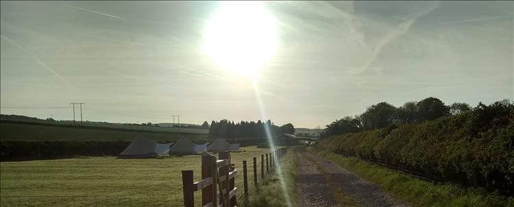 The low sun shines in clear skies over a farm track with Teepees and trees nearby