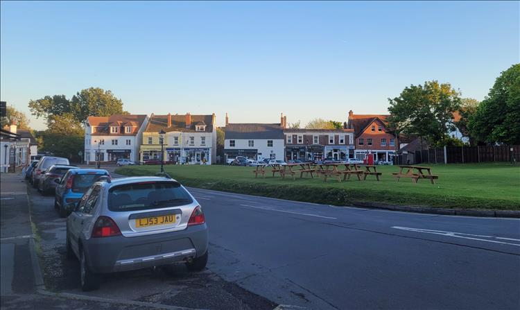 a village green with a few shops and houses around the edges with clear skies