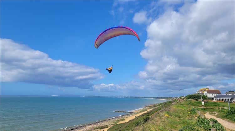A man hangs for his large paraglider over the bluffs. Blue skies and the sea