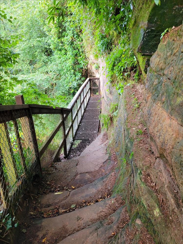 A narrow wooden and metal path clings to the side of the rocks leading to the cave