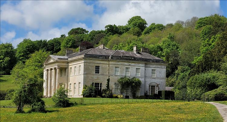 A large mansion house from the early 19th centuary in an open field with trees behind