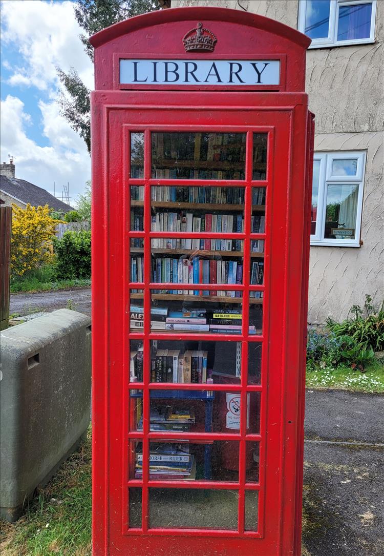 An old red phone box is now a tiny library filled with books on shelves