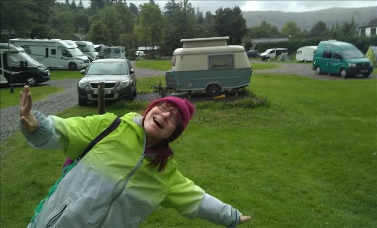 Sharon smiling and larking around on a campsite in the rain