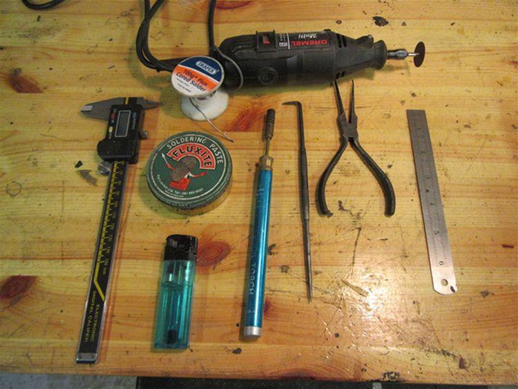 On the bench we see measuring callipers, solder, Dremel, pliers, scribe, soldering iron and flux