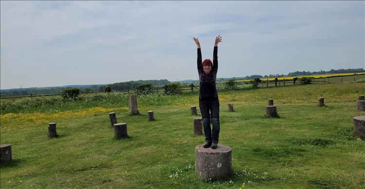 Sharon stands on a concrete stump and stretches to the skies while smiling