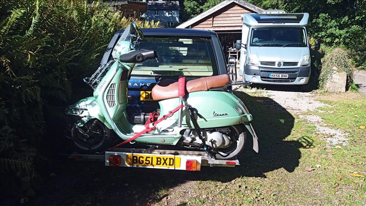 A light green Vespa 200 on a rack fitted to the tow bar of a Range Rover car