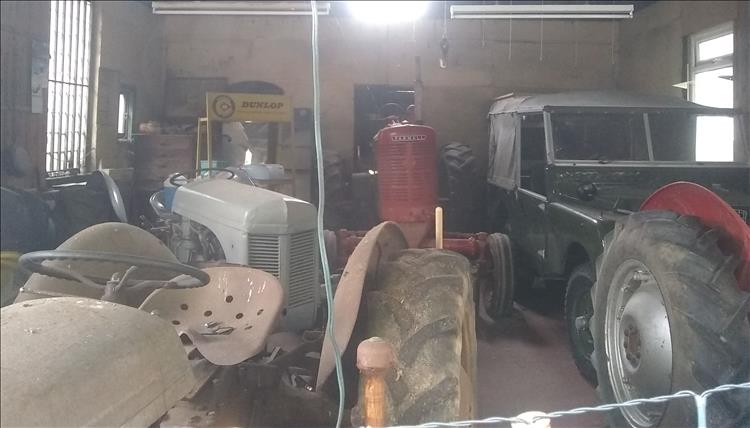 Several vintage tractors seen through the dusty window of an old shop