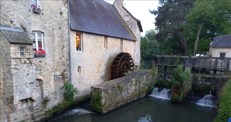 A large stone building, a waterwheel and the river in Bayeux