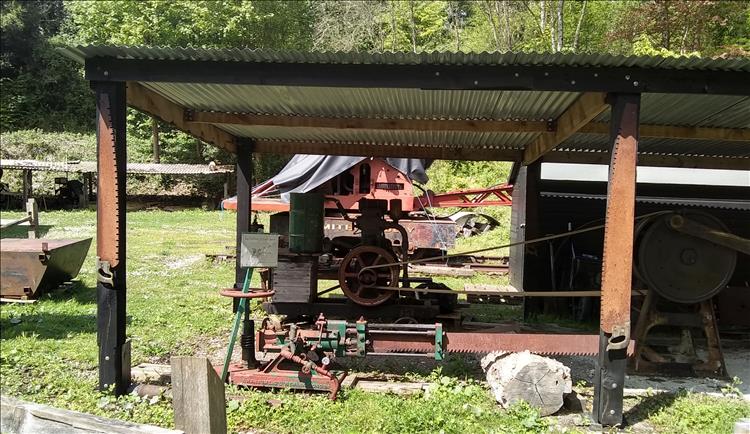 An old engine powering a wood saw and a steam crane in the background